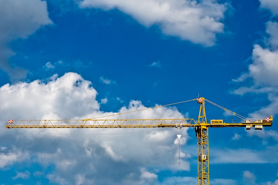A construction crane set against a bright blue sky with fluffy clouds.