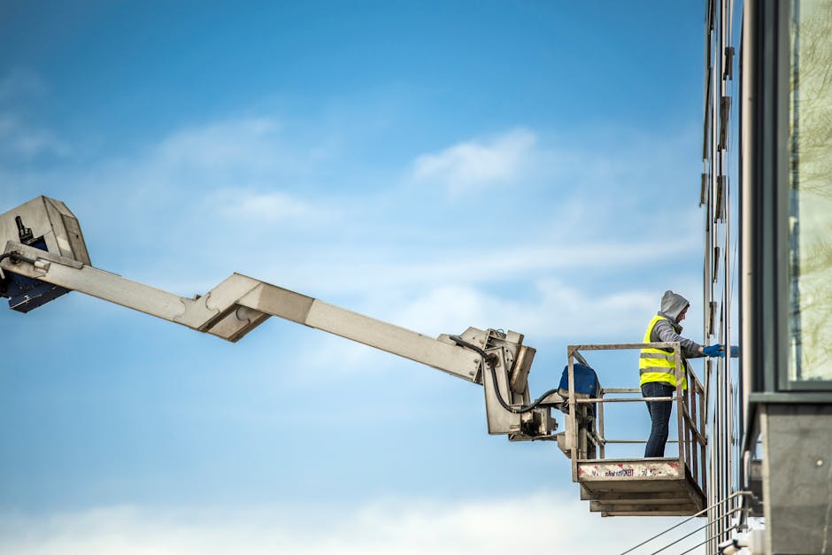 A construction worker cleans glass windows on a high-rise building using an industrial lift.