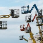 A collection of colorful boom lifts reaching toward a clear blue sky, showcasing industrial machinery.