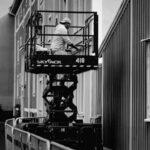 Black and white photo of a worker on a lift performing maintenance on a building's exterior.