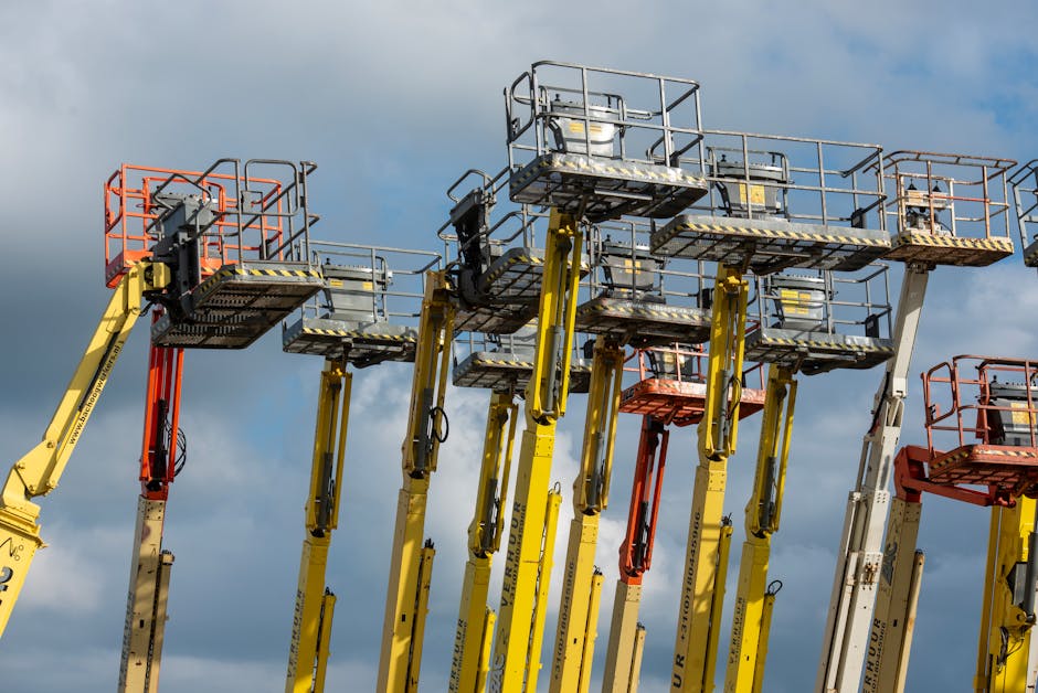 Multiple aerial work platforms with colorful booms reaching skyward against a cloud-dotted backdrop.