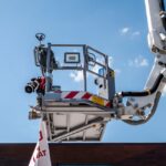 Firefighting ladder truck equipped with water cannon and hose against blue sky.