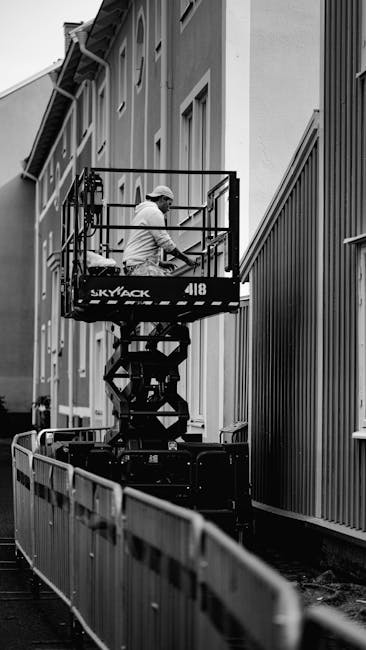 Black and white photo of a worker on a lift performing maintenance on a building's exterior.