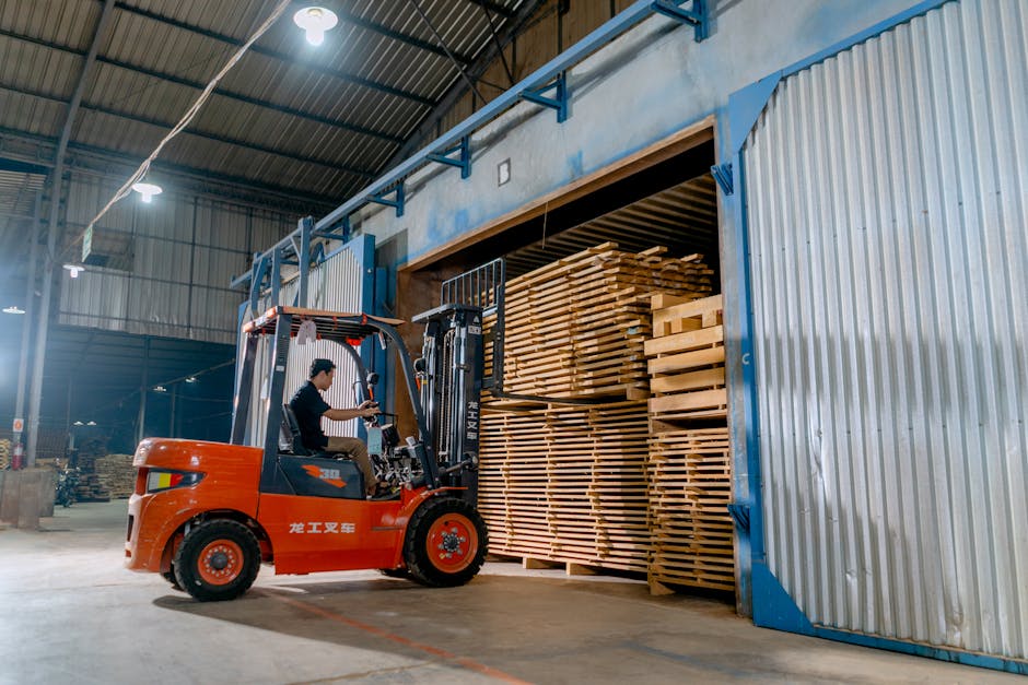 Man operating a forklift indoors loading wooden pallets in a warehouse.