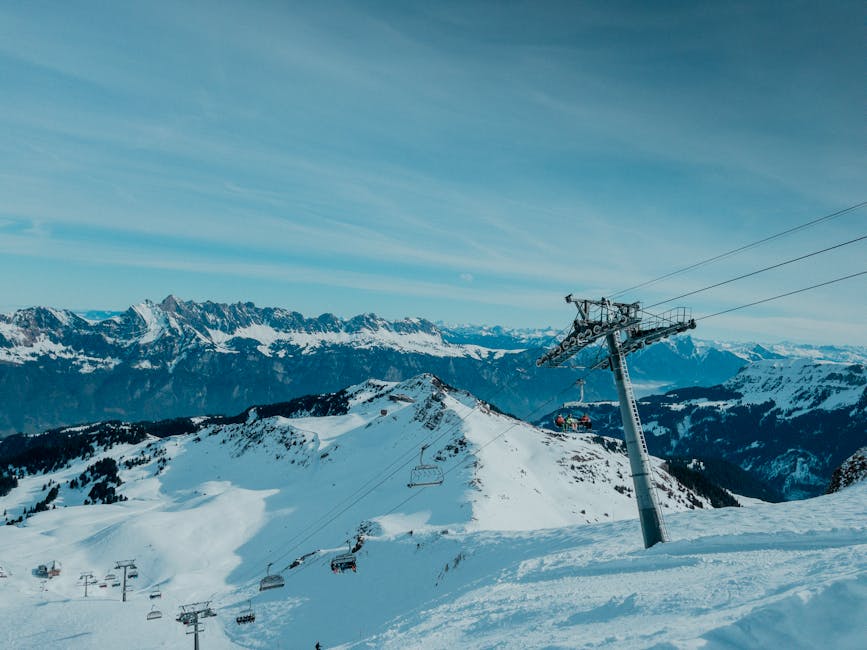 Breathtaking view of a snow-covered mountain range with ski lift and clear blue sky.
