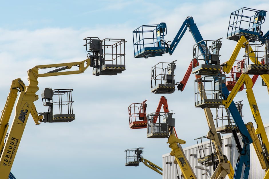 A collection of colorful boom lifts reaching toward a clear blue sky, showcasing industrial machinery.