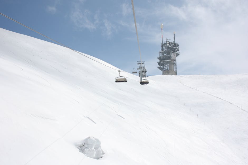 Ski lift on snowy slope with communication tower against blue sky.